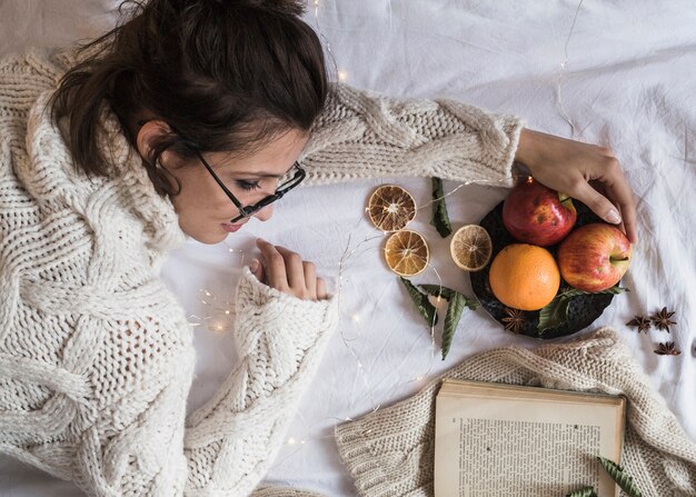 Junge Frau, die auf Decke mit Platte von Früchten liegt