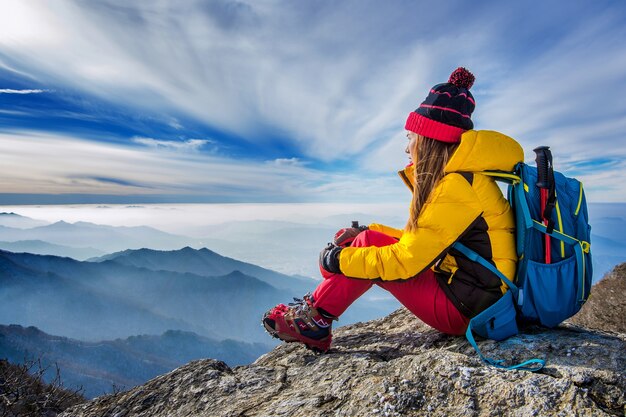 Junge Frau, die auf dem Hügel der hohen Berge sitzt