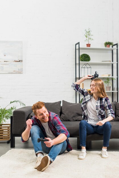 Junge Frau, die auf dem Sofa schlägt ihren Freund mit Steuerknüppel sitzt