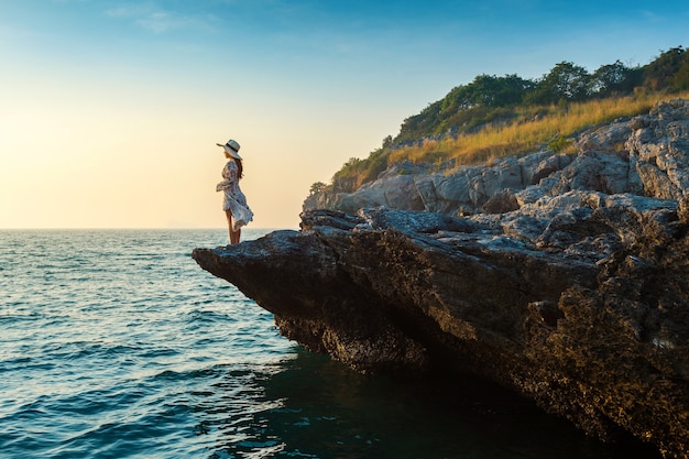 Junge Frau, die auf der Spitze des Felsens steht und die Küste und den Sonnenuntergang in Si Chang Insel betrachtet.