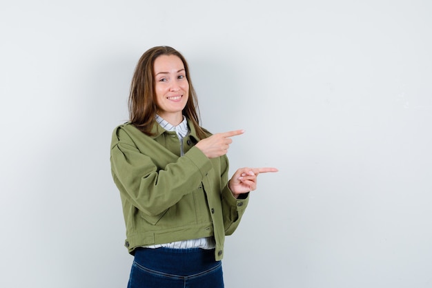 Junge Frau, die auf die rechte Seite in Hemd, Jacke zeigt und optimistisch schaut, Vorderansicht.