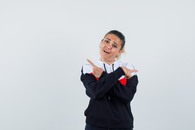 Junge Frau, die auf die Rückseite im bunten Sweatshirt zeigt und verwirrt schaut, Vorderansicht.