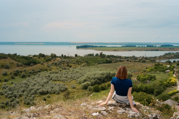 Kostenloses Foto junge frau, die auf einem felsen sitzt und einen friedlichen moment genießt.