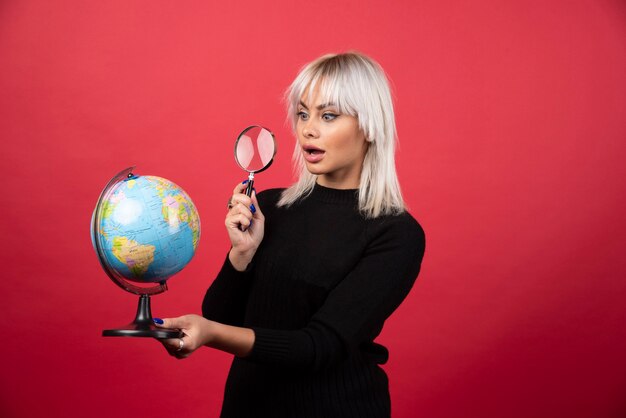 Junge Frau, die auf einem Globus mit Lupe auf einem roten Hintergrund schaut