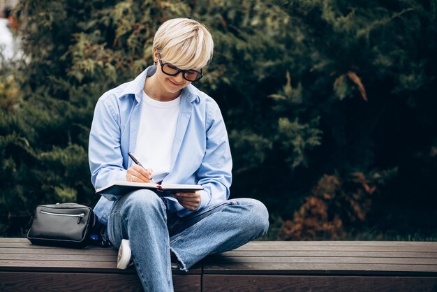 Junge Frau, die auf einer Bank sitzt und in ein Notizbuch schreibt