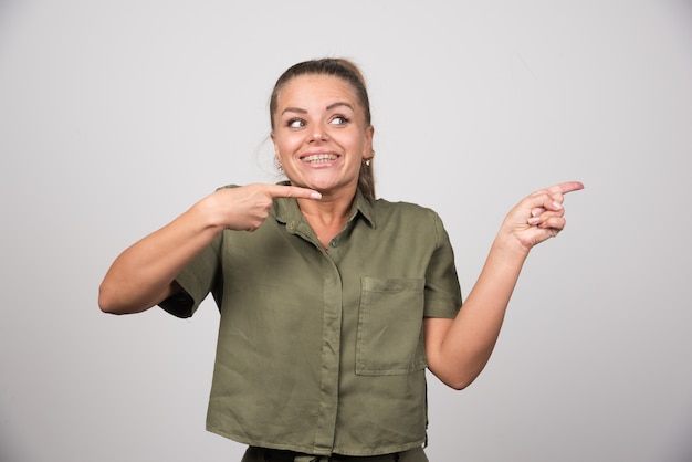 Junge Frau, die auf etwas auf grauer Wand zeigt.