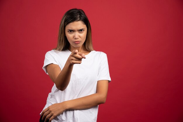 Junge Frau, die auf etwas auf roter Wand zeigt.