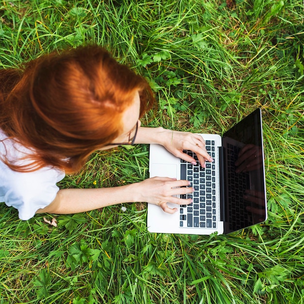 Junge Frau, die auf Gras mit Laptop liegt