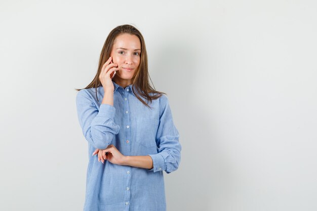 Junge Frau, die auf Handy spricht und im blauen Hemd lächelt