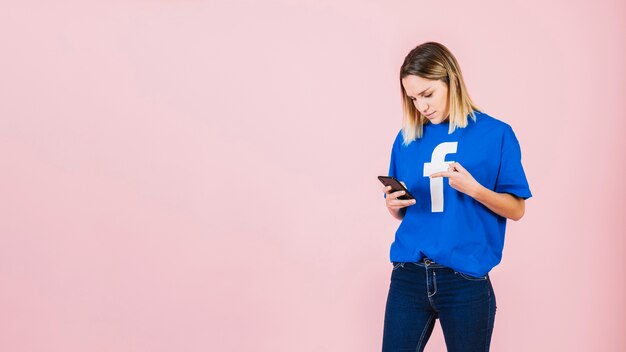 Junge Frau, die auf Handy über rosa Hintergrund zeigt