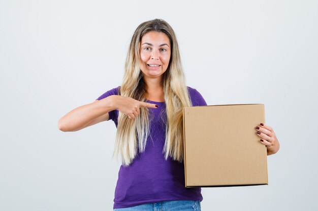 Junge Frau, die auf Kasten im violetten T-Shirt zeigt und aufmerksam schaut. Vorderansicht.