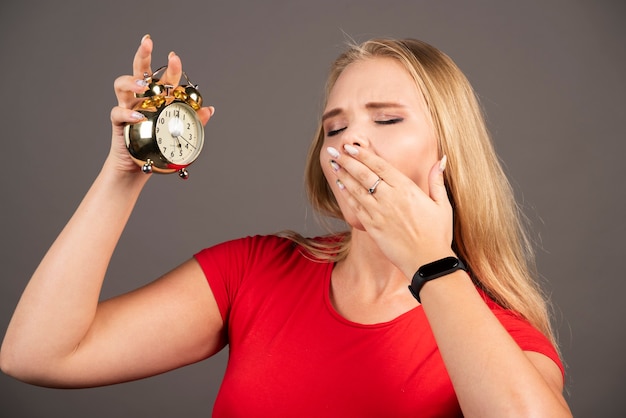 Junge Frau, die auf schwarzer Wand mit Uhr gähnt.