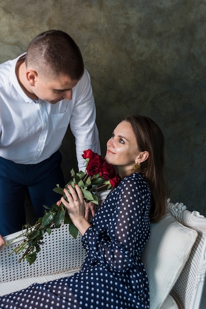 Kostenloses Foto junge frau, die auf sofa mit blumen sitzt