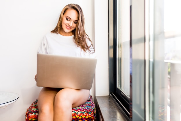 Junge Frau, die auf Stuhl mit Laptop zu Hause sitzt