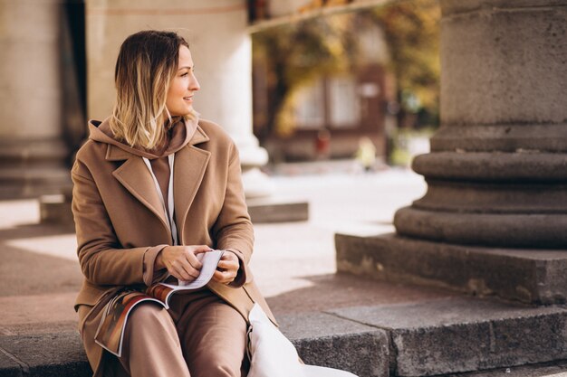 Junge Frau, die auf Treppen in der Stadt sitzt und Zeitschrift liest