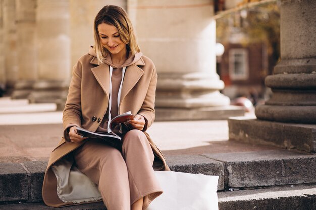 Junge Frau, die auf Treppen in der Stadt sitzt und Zeitschrift liest