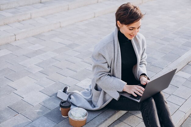 Junge Frau, die auf Treppen sitzt und am Computer arbeitet