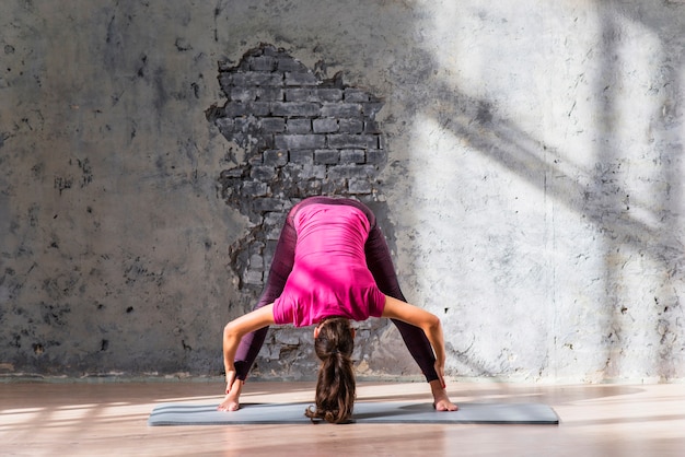 Junge Frau, die auf übendem Yoga der Übungsmatte steht