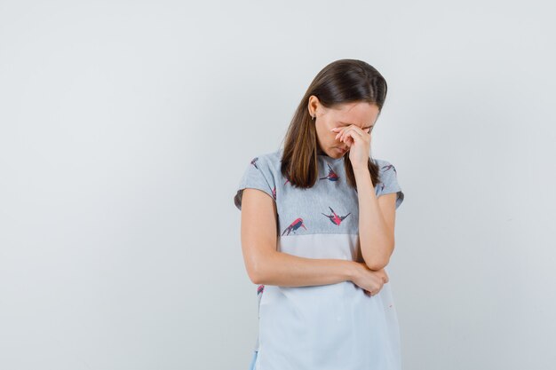 Junge Frau, die Augen mit Hand im T-Shirt bedeckt und müde schaut. Vorderansicht.