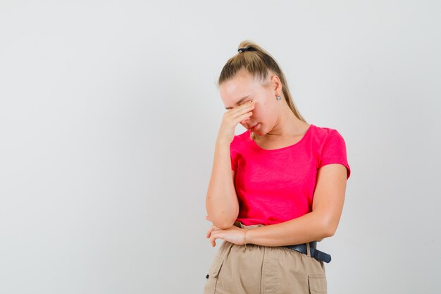 Junge Frau, die Augen und Nase im T-Shirt und in der Hose reibt und müde aussieht