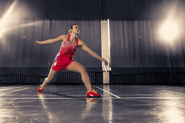 Junge Frau, die Badminton über Turnhalle spielt