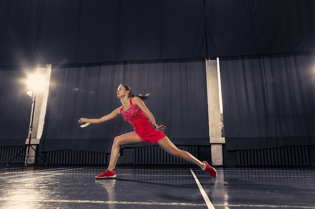 Junge Frau, die Badminton über Turnhalle spielt