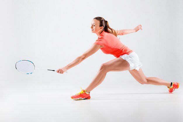 Junge Frau, die Badminton über weißer Wand spielt