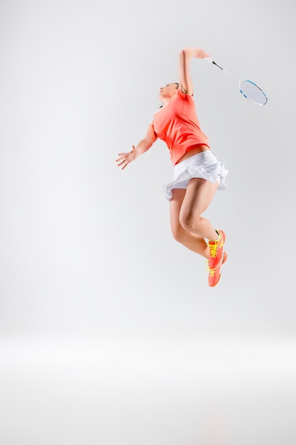 Junge Frau, die Badminton über weißer Wand spielt