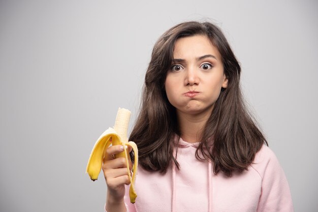 Junge Frau, die Banane über grauer Wand isst.