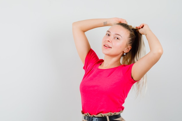 Junge Frau, die beim Ziehen des Haares im T-Shirt aufwirft und faszinierend schaut