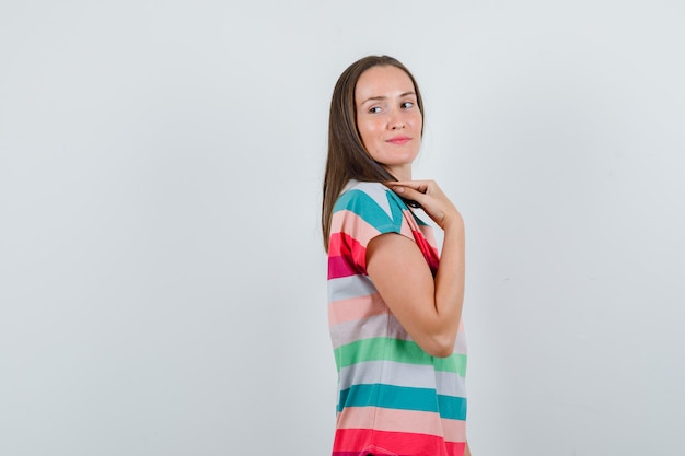 Junge Frau, die beim Zurückblicken im T-Shirt aufwirft und charmant schaut. .