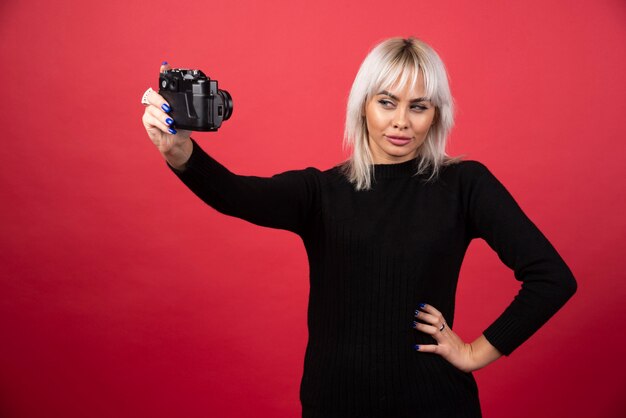 Junge Frau, die Bilder mit einer Kamera auf einem roten Hintergrund nimmt. Hochwertiges Foto