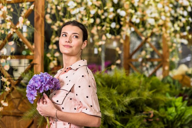 Junge Frau, die blaue Blume im grünen Haus hält