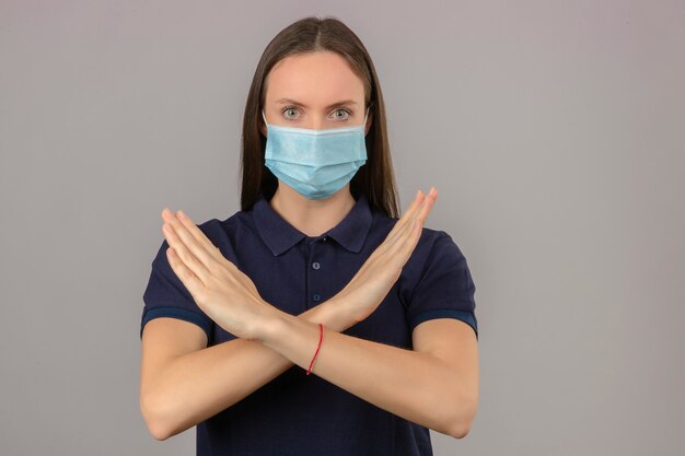 Kostenloses Foto junge frau, die blaues poloshirt in der medizinischen schutzmaske trägt, die stoppgeste mit ernstem gesicht auf lokalisiertem hellgrauem hintergrund macht