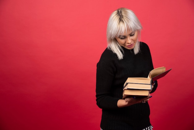 Junge Frau, die Bücher an einer roten Wand hält.