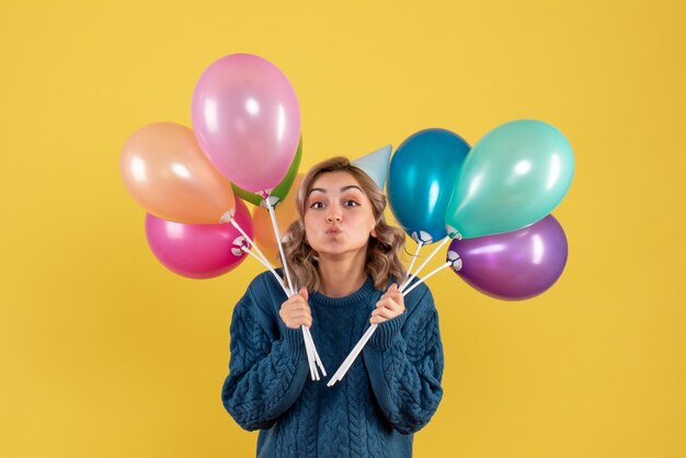 junge Frau, die bunte Luftballons auf Gelb hält