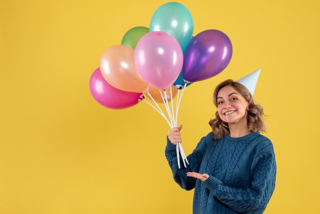 junge Frau, die bunte Luftballons auf Gelb hält