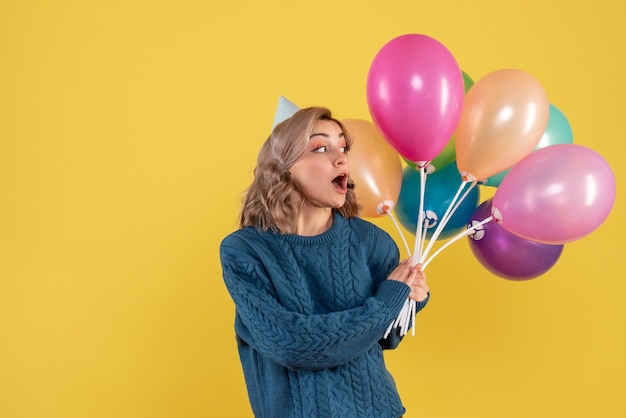 junge Frau, die bunte Luftballons auf Gelb hält