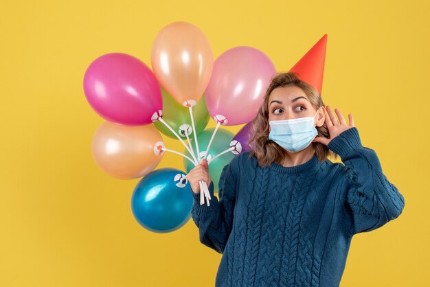 junge Frau, die bunte Luftballons auf Gelb hält