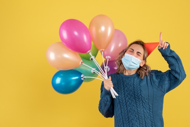 junge Frau, die bunte Luftballons auf Gelb hält