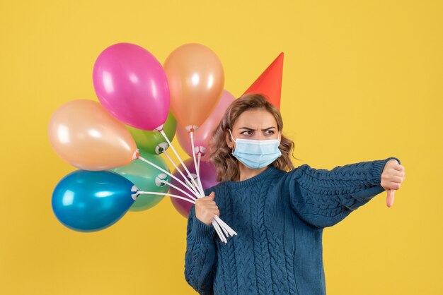 junge Frau, die bunte Luftballons auf Gelb hält