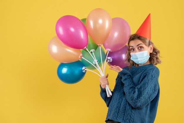 junge Frau, die bunte Luftballons auf Gelb hält