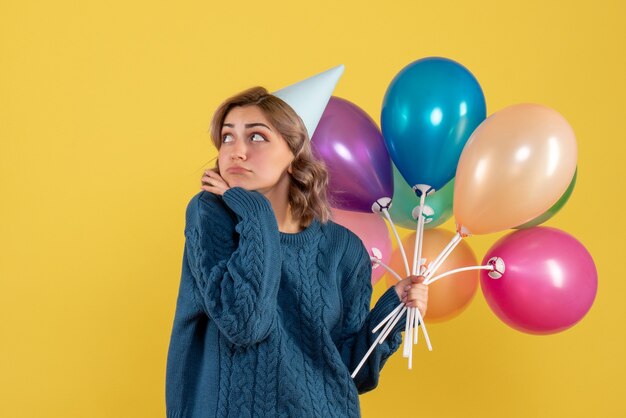 junge Frau, die bunte Luftballons auf Gelb hält