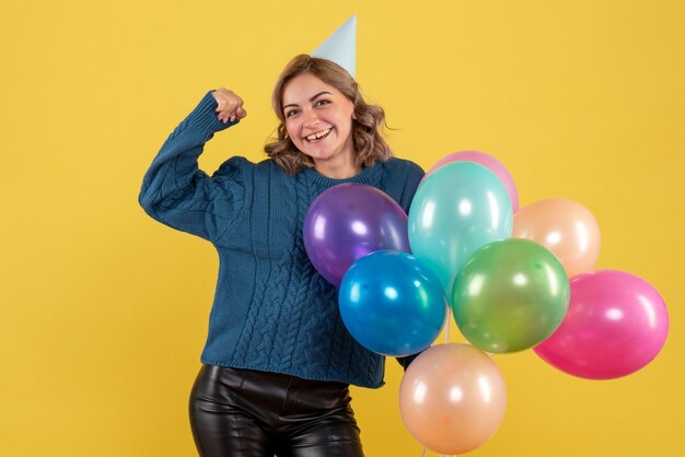 junge Frau, die bunte Luftballons auf Gelb hält