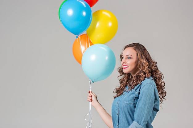 Junge Frau, die bunte Luftballons auf grauer Studiowand hält