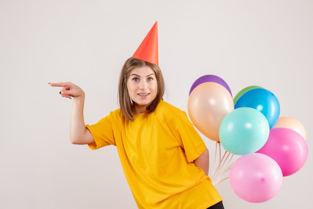 junge Frau, die bunte Luftballons hinter ihrem Rücken auf Weiß versteckt