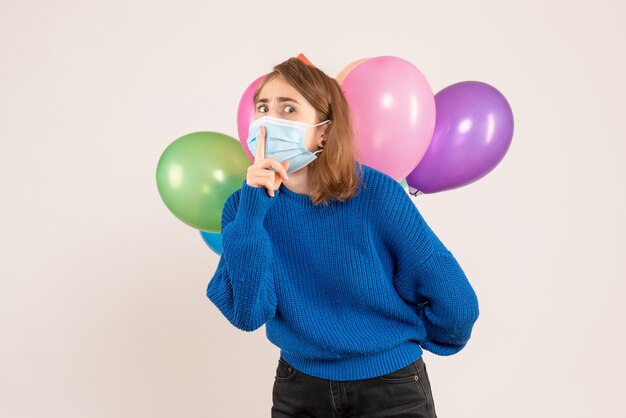 junge Frau, die bunte Luftballons hinter ihrem Rücken auf Weiß versteckt