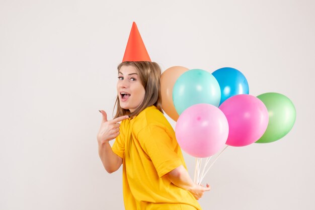 junge Frau, die bunte Luftballons hinter ihrem Rücken auf Weiß versteckt