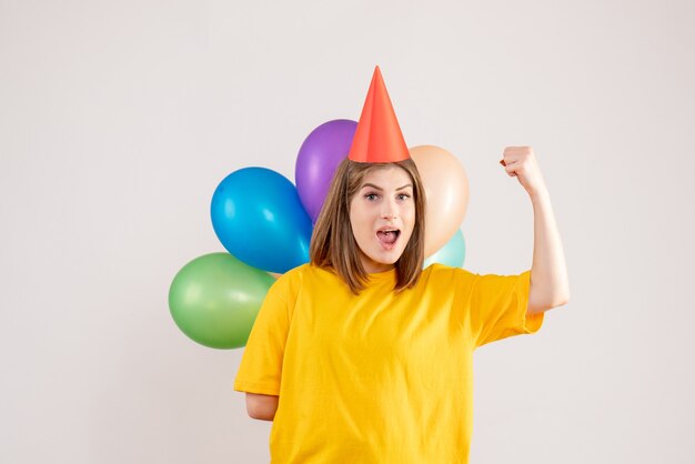 junge Frau, die bunte Luftballons hinter ihrem Rücken auf Weiß versteckt