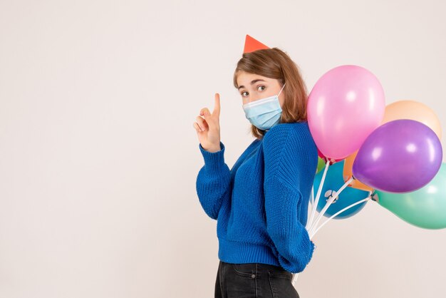 junge Frau, die bunte Luftballons hinter ihrem Rücken auf Weiß versteckt